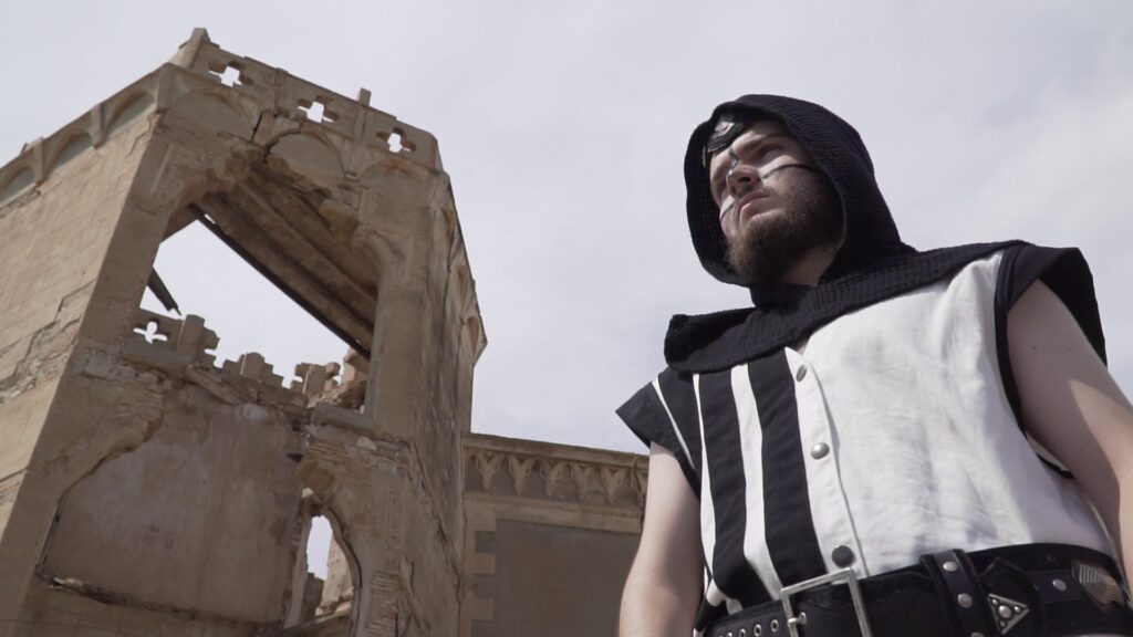 Festero con traje blanco y negro junto a una construcción histórica en ruinas.