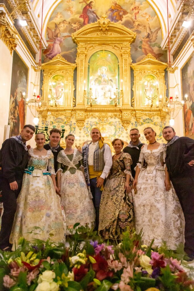 Grupo de festeros con trajes de gala ante el altar de una iglesia.