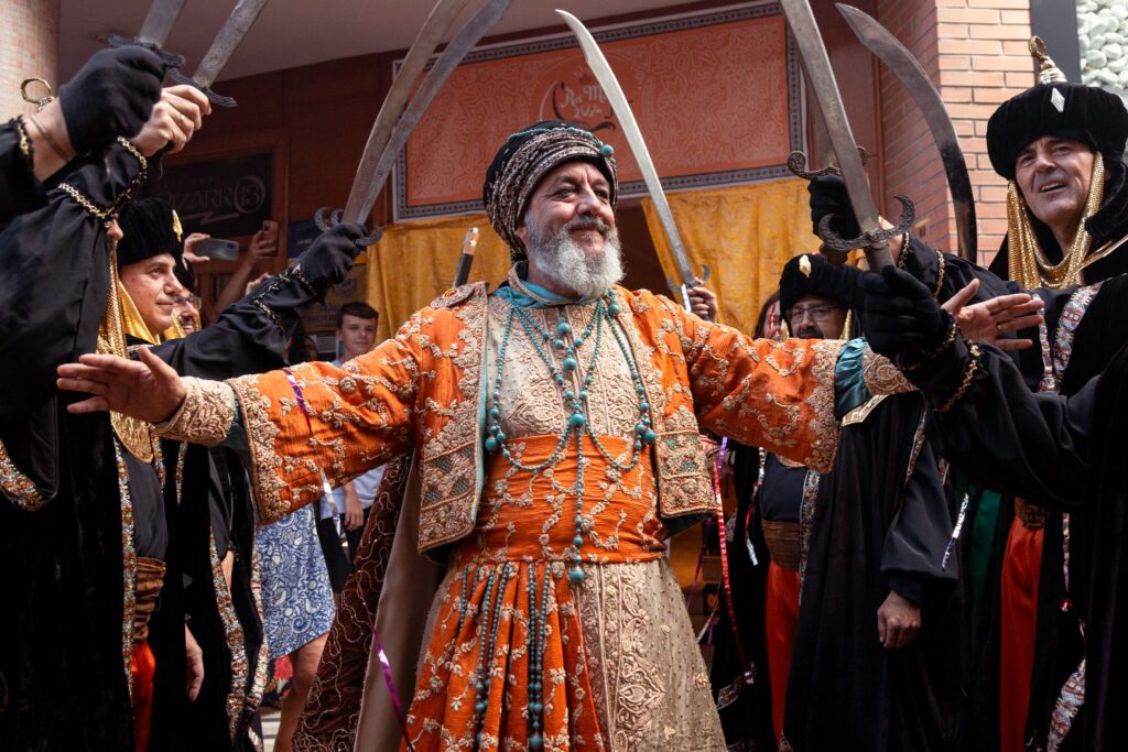 Rey moro con traje naranja rodeado de festeros con espadas curvas.