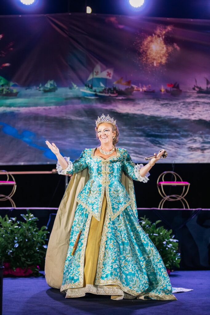 Reina con corona y vestido turquesa y dorado en el escenario de las fiestas de Villajoyosa.